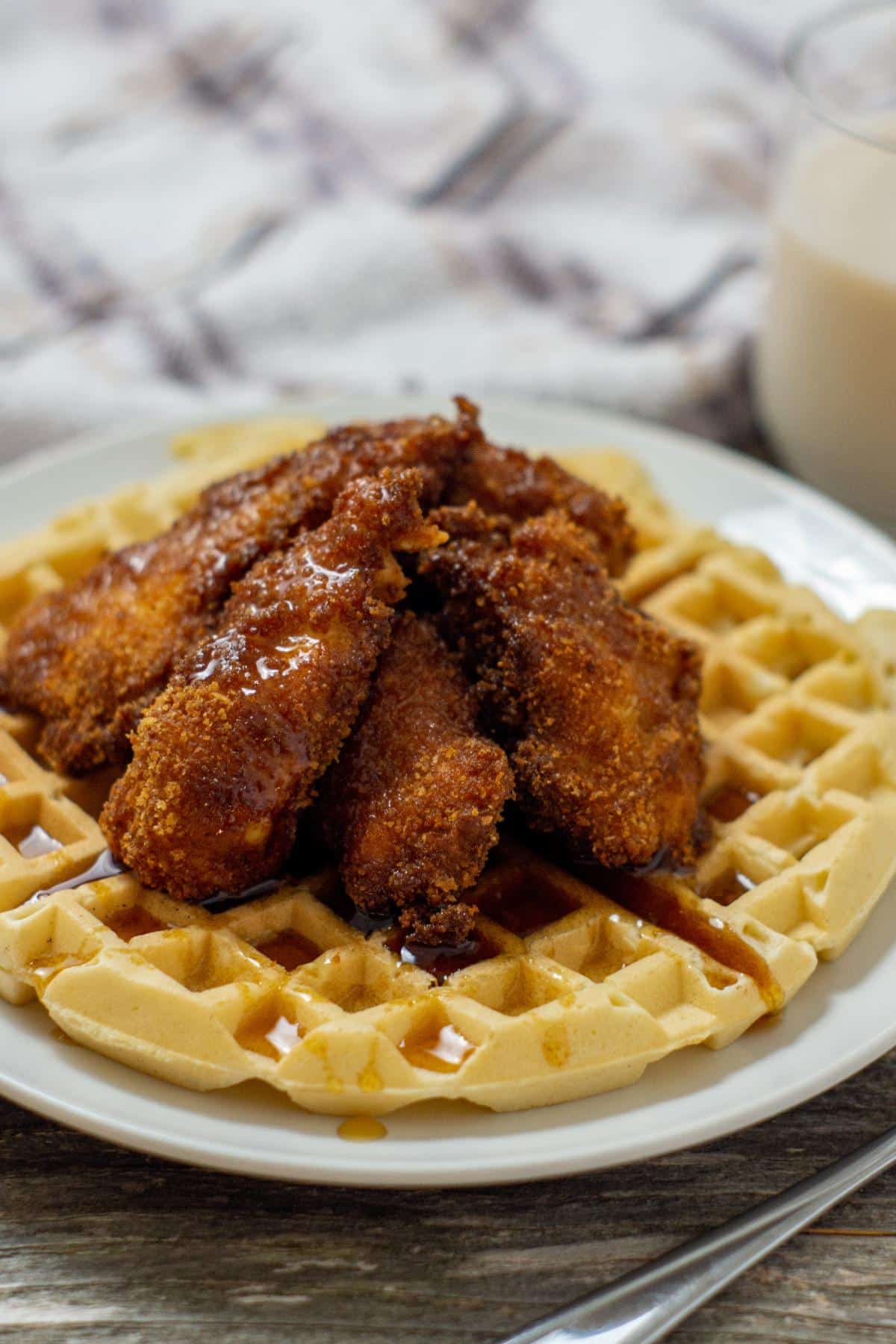 Southern Chicken and Waffles with maple syrup on a serving plate next to a glass of milk.