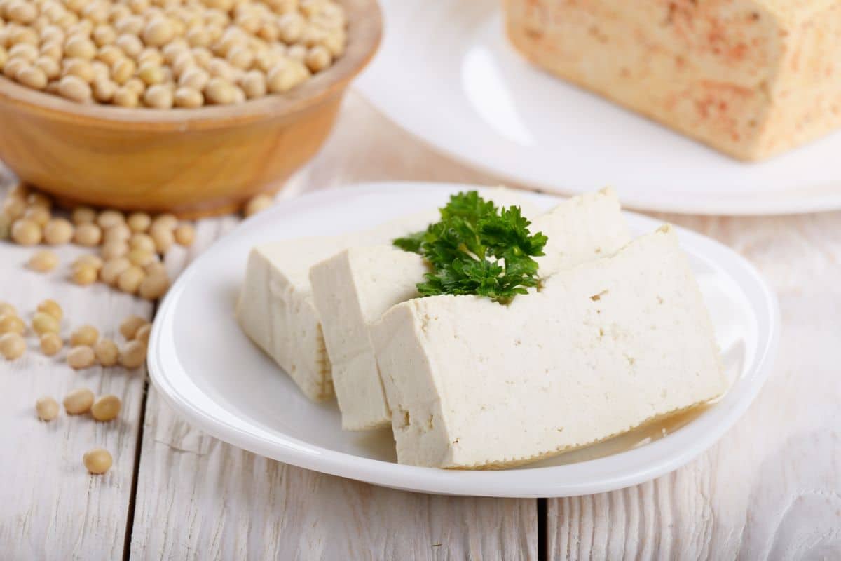 Tofu, a substitute for goat cheese, on a plate next to a bowl of soybeans.