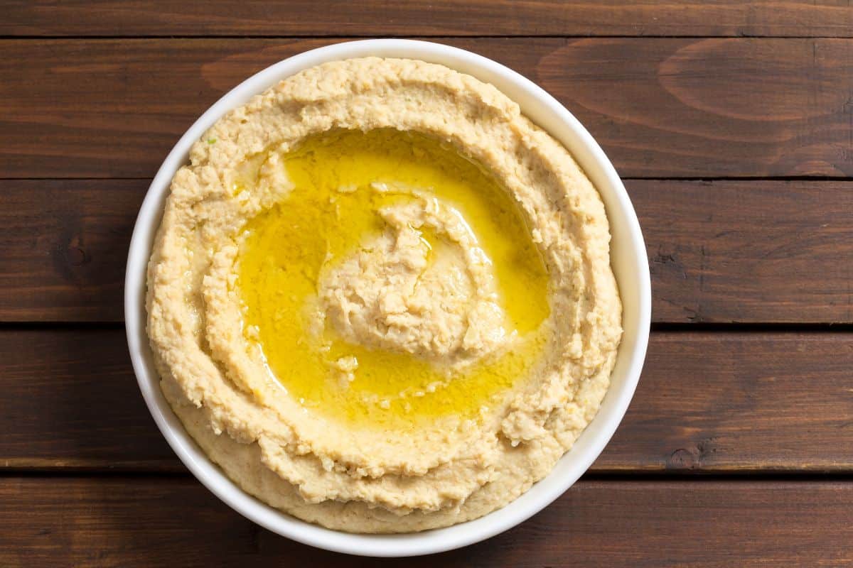 A bowl of hummus, a perfect substitute for goat cheese, on a wooden table.