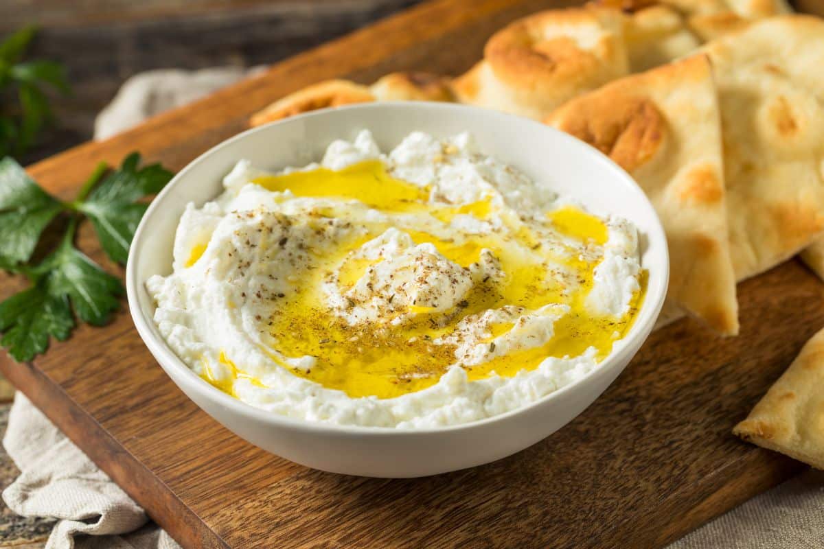 A bowl of Labneh with pita bread on a wooden cutting board, a delicious and creamy substitute for goat cheese.