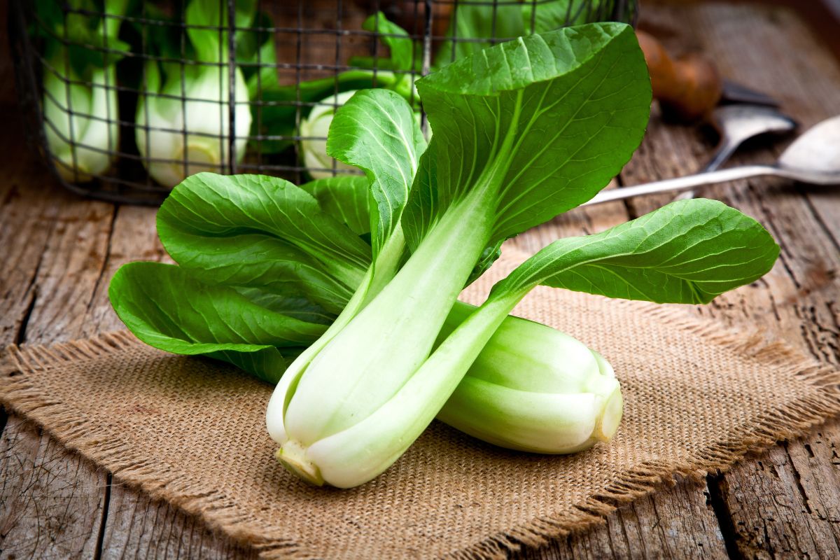 Bok choy leaves in a basket and on a burlap cloth on a wooden table.