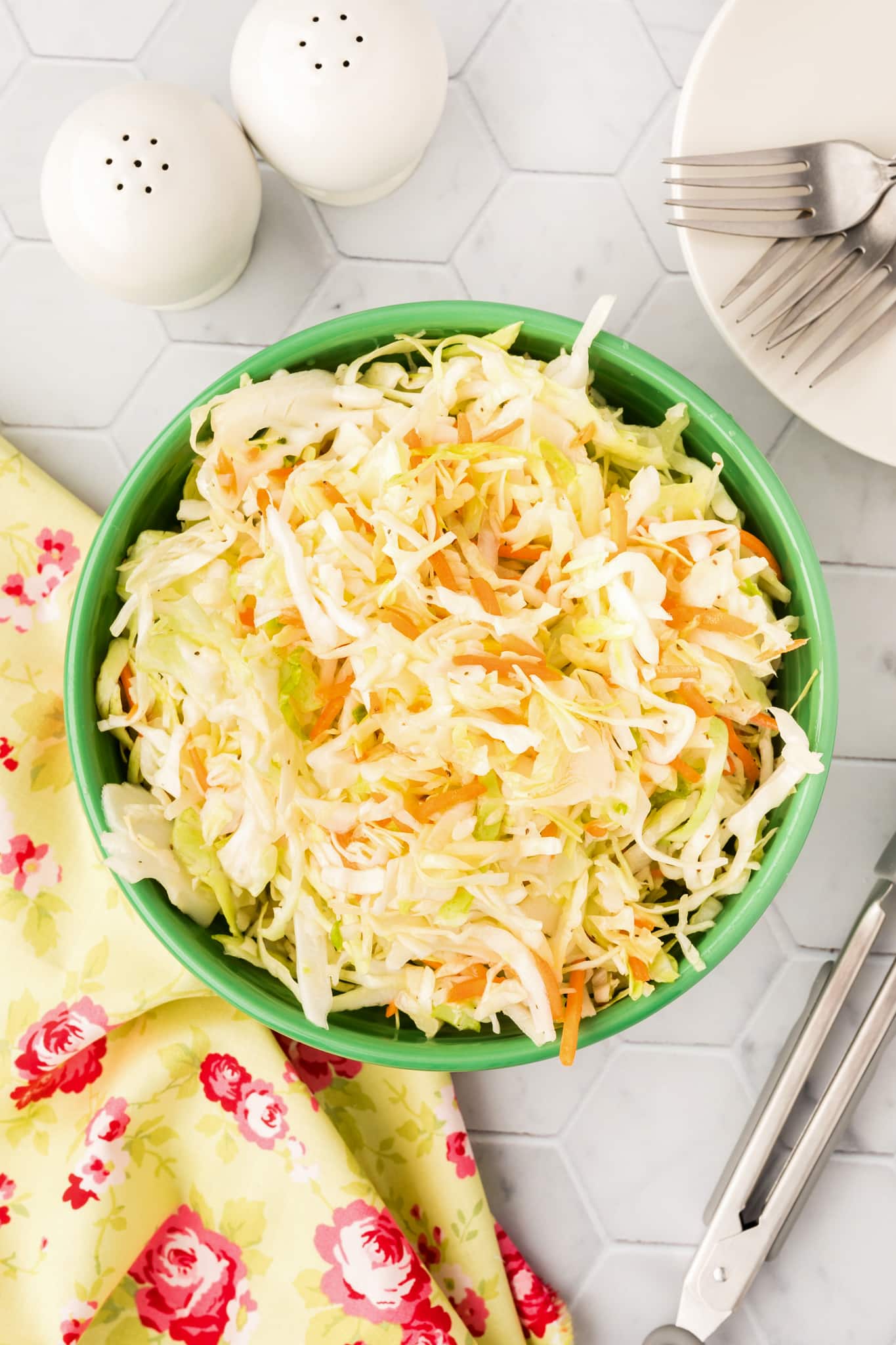 Coleslaw in a green bowl next to a fork and spoon.