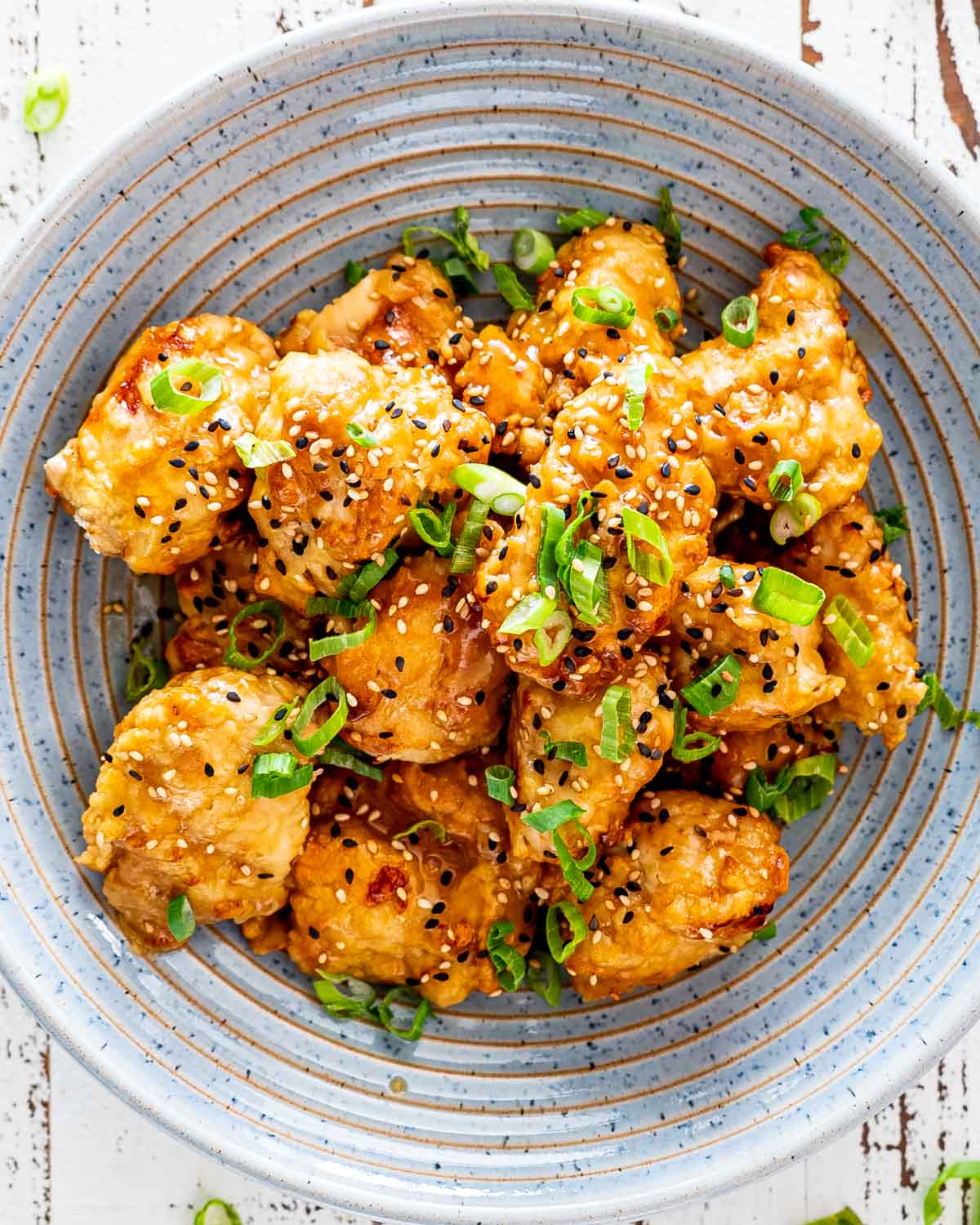 A bowl of sesame chicken with sesame seeds.