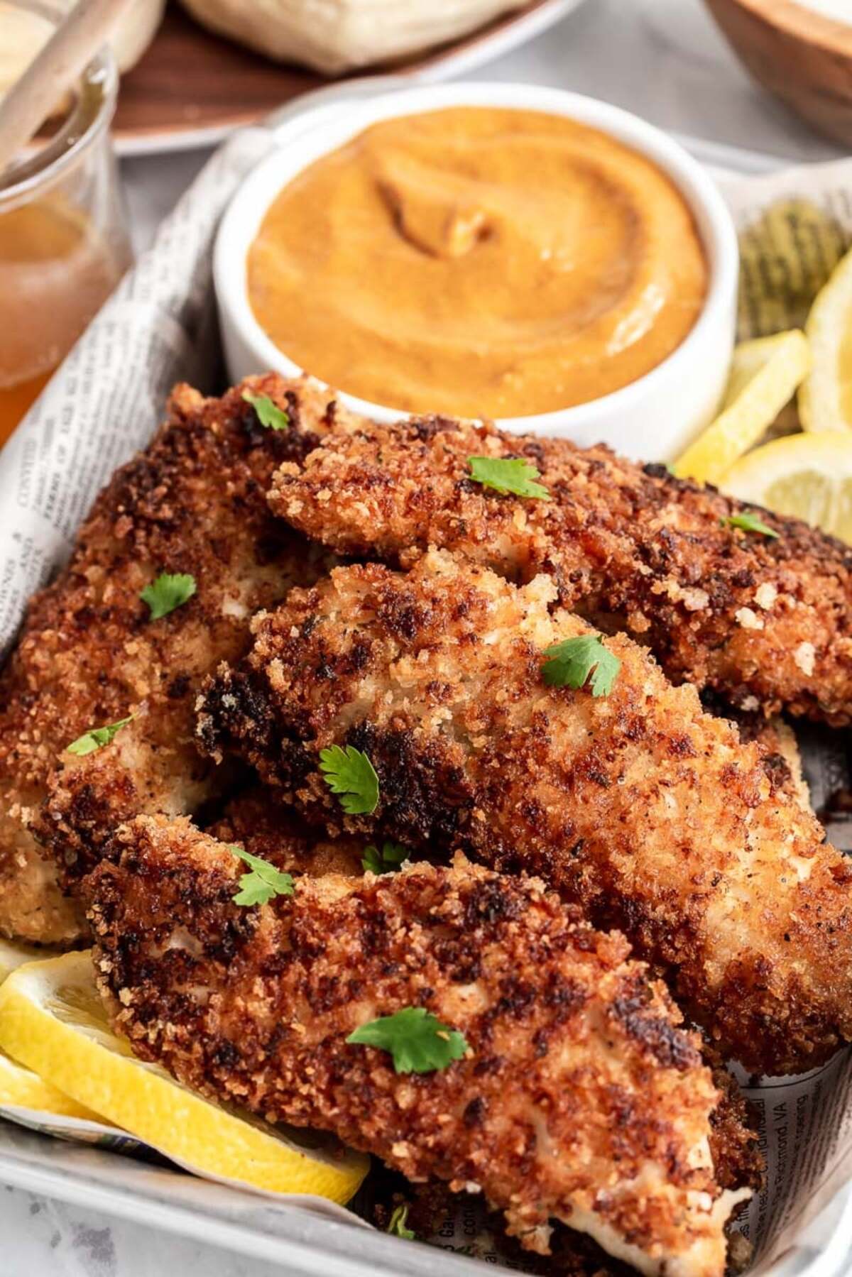 A tray of fried chicken fingers with dipping sauce and lemon wedges.