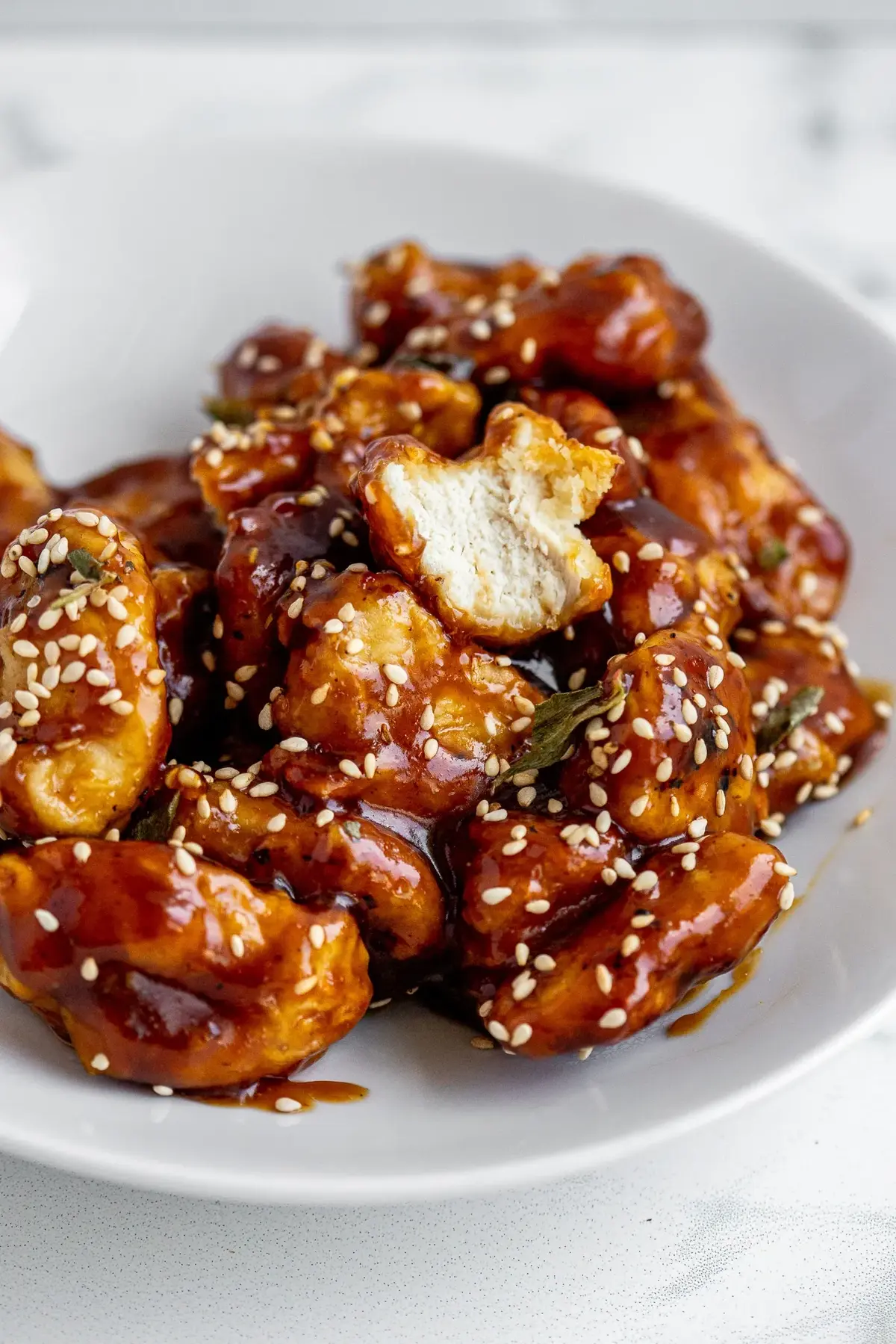 Sesame chicken on a white plate with sesame seeds.
