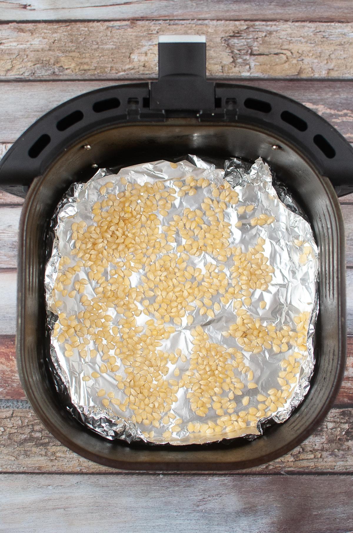 Popcorn kernels arranged on aluminum foil in an air fryer.
