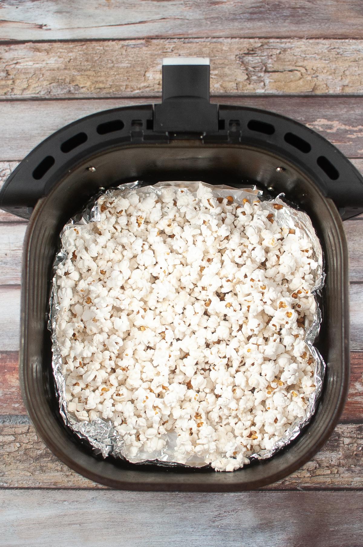 Air fryer popcorn filling a basket on a wooden surface.
