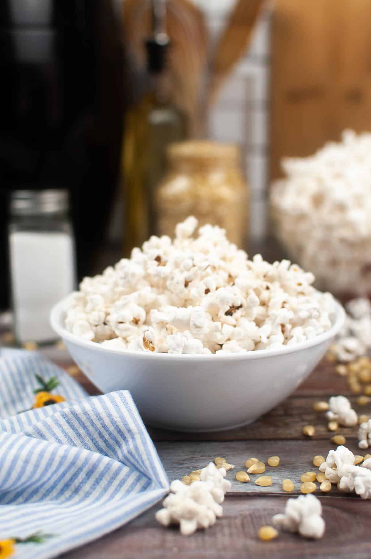 A bowl of air fryer popcorn with kernels scattered around on a wooden surface.