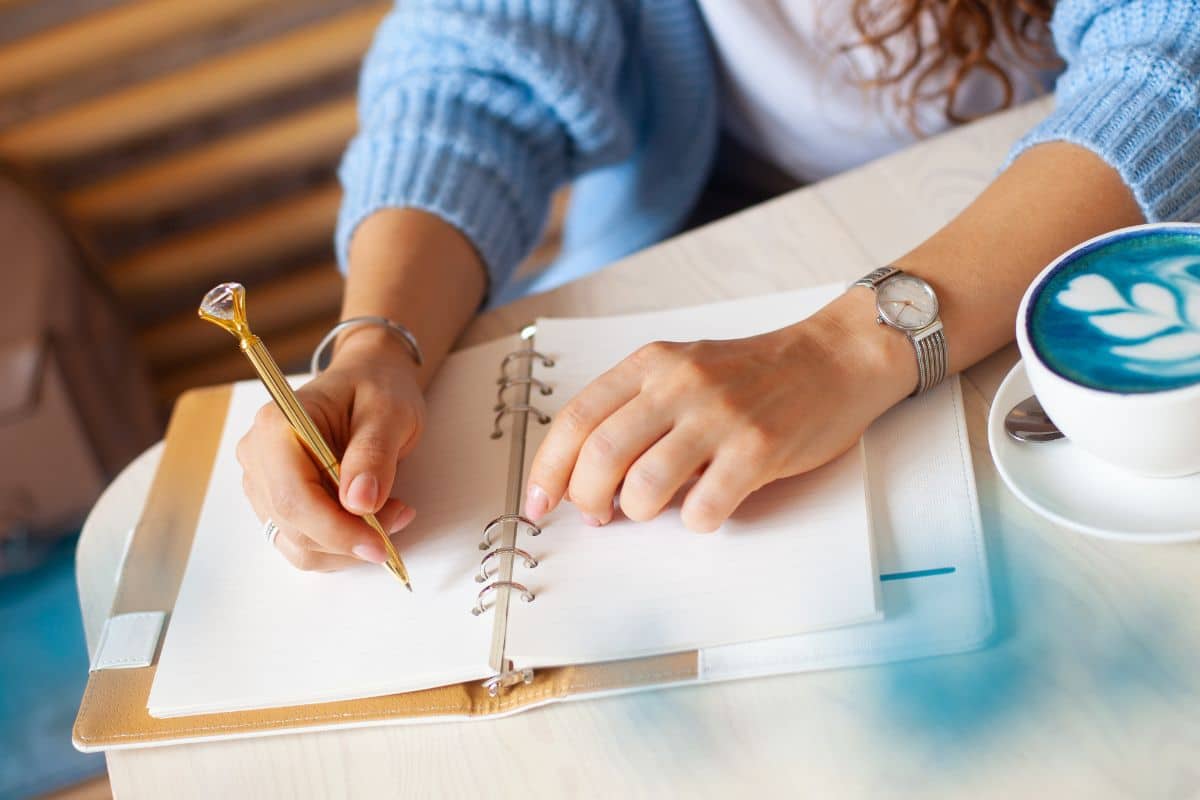 A person jotting down journal ideas for teens in a notebook with a pen.