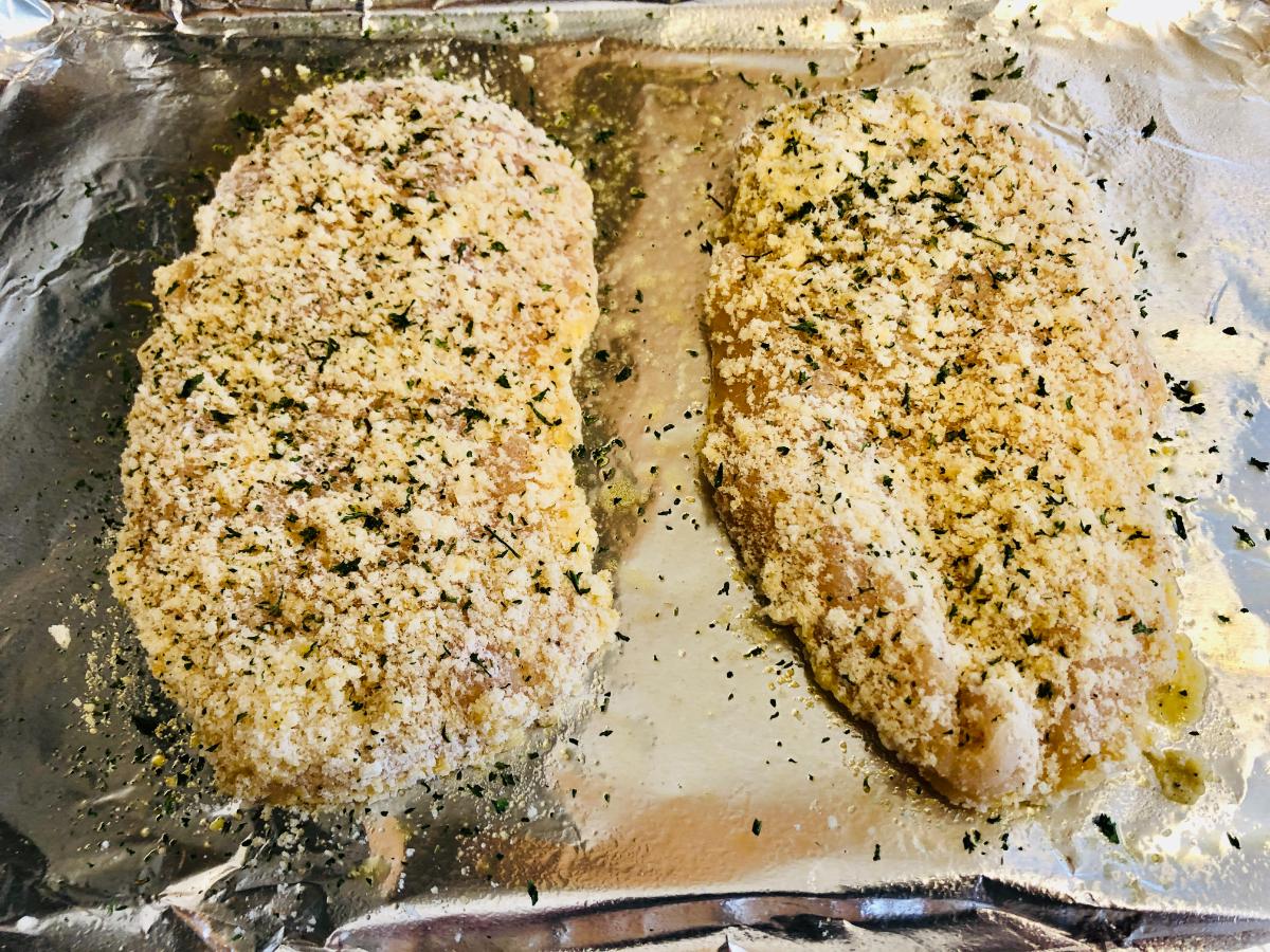 Two pieces of breaded chicken breast fillet arranged on a baking sheet.