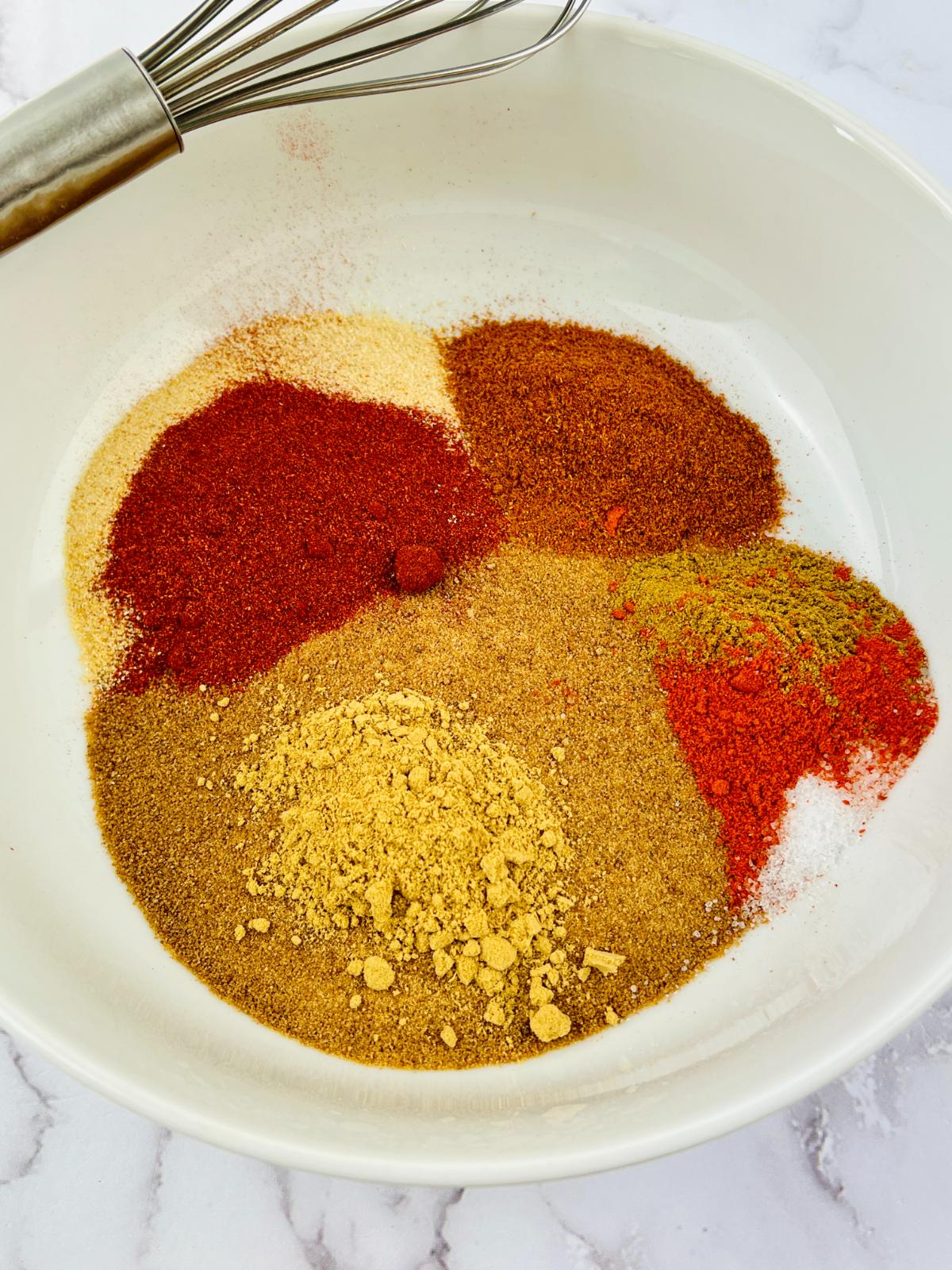 A whisk sits in a bowl of spices, perfect for making a dry rub for pork.
