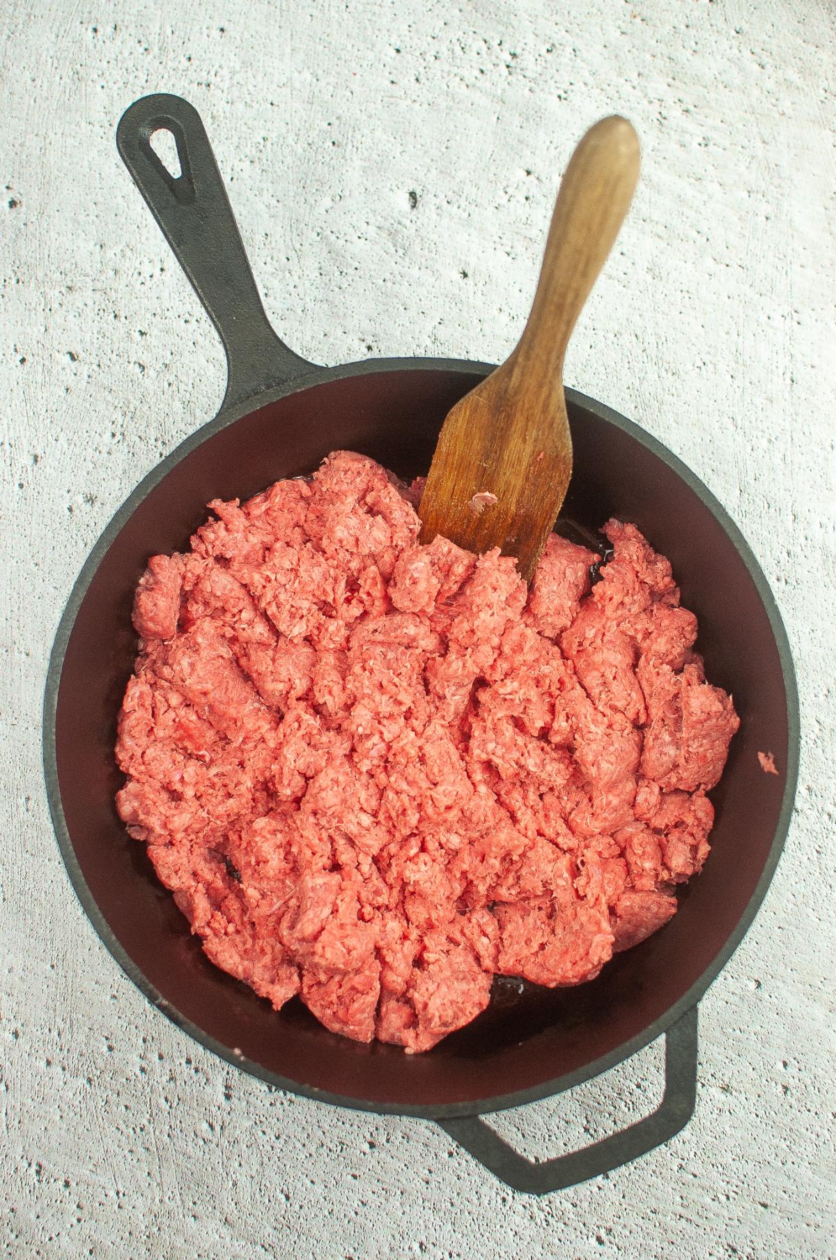 Ground beef cooking in a Dutch oven with wooden spoon in it.