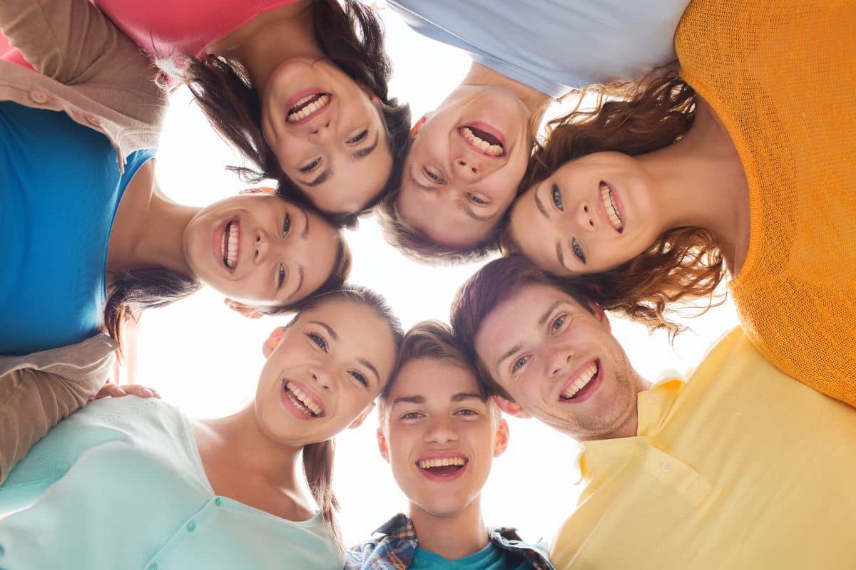 A group of young people standing together in a circle looking down at the camera.