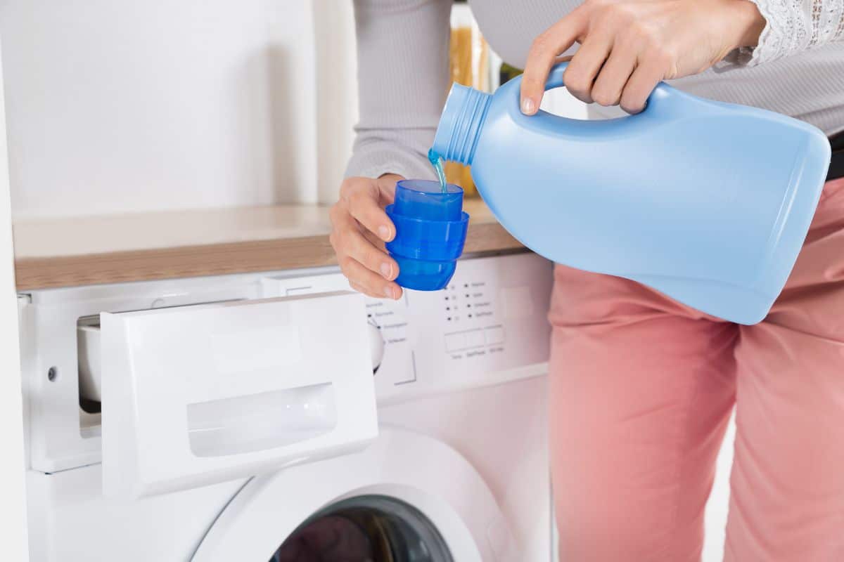 A woman pouring laundry detergent into a blue cup to wash clothes.