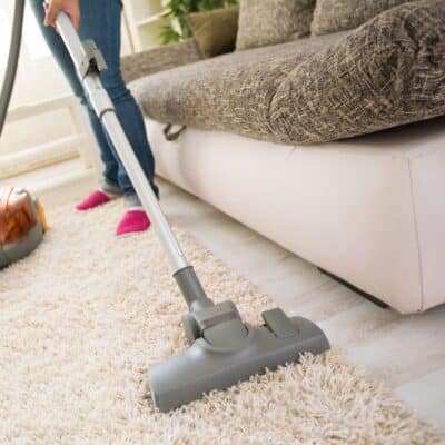 In this scenario, a woman is diligently vacuuming a carpet to effectively remove any dirt and debris.