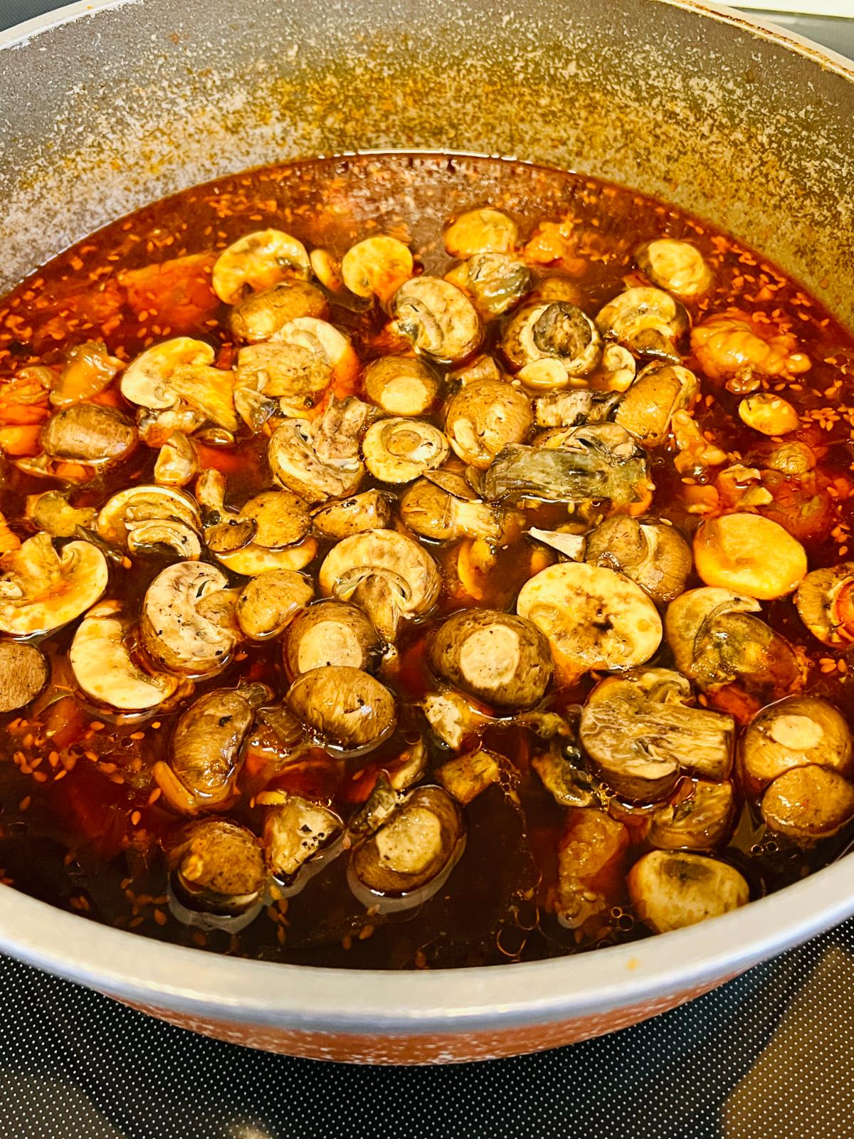 Sliced mushrooms simmering in a savory Korean beef stew broth in a cooking pot.