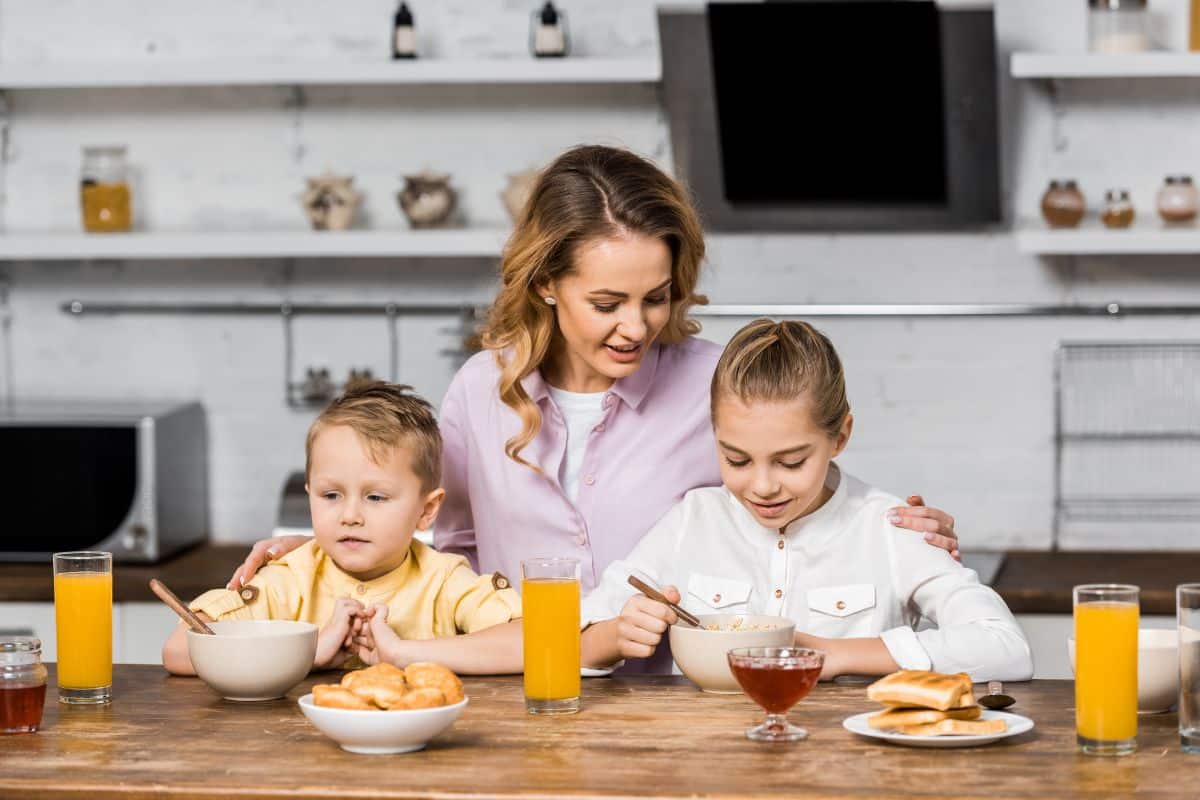 A mother is teaching her children to eat properly in the kitchen.