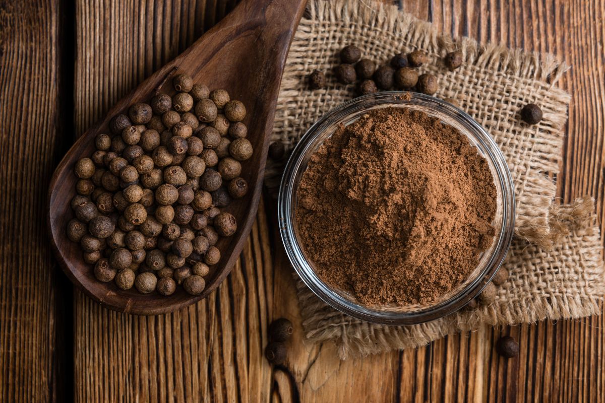 Allspice seed and powder on a wooden spoon and in a glass bowl on a wooden table.