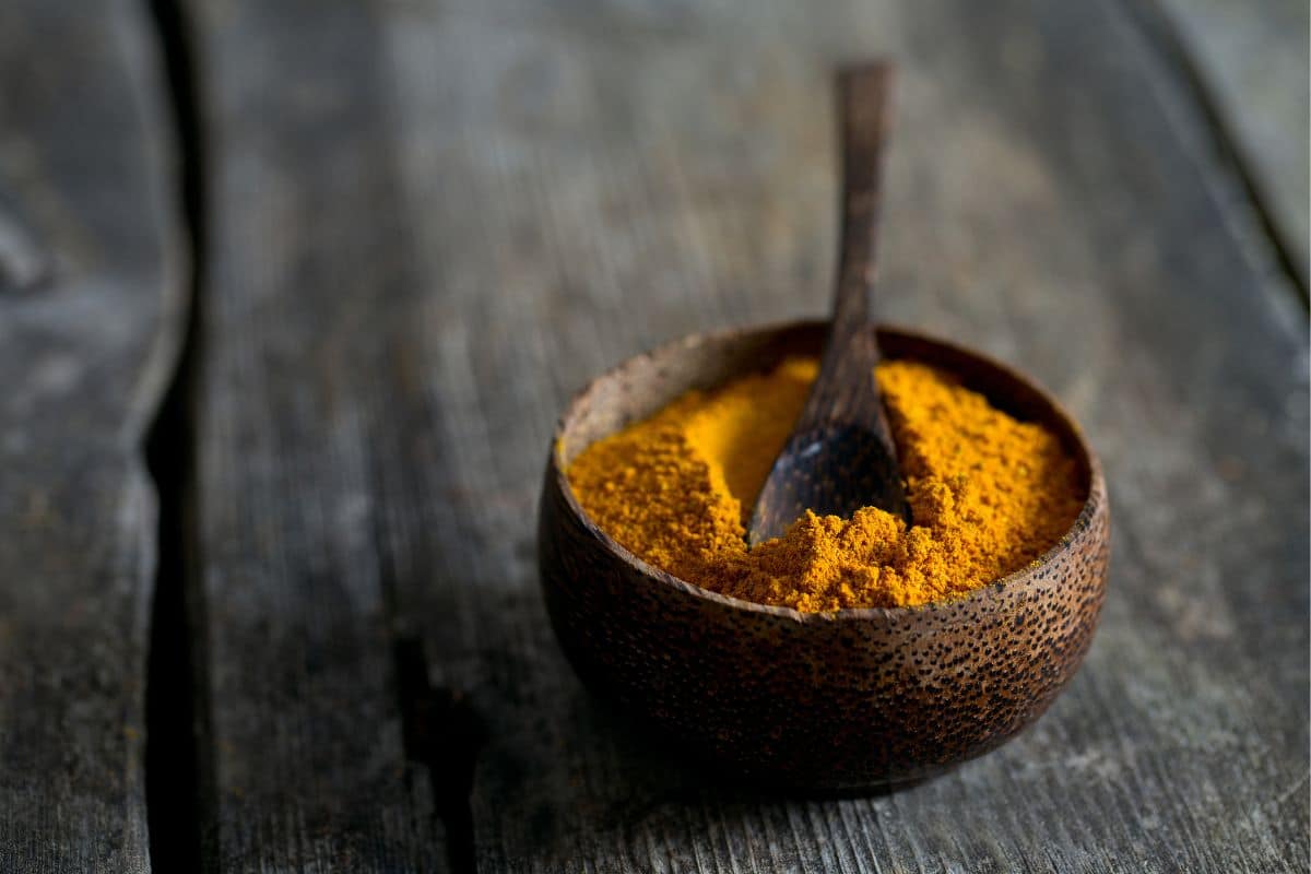 Curry powder in a wooden bowl with spoon on a wooden table.