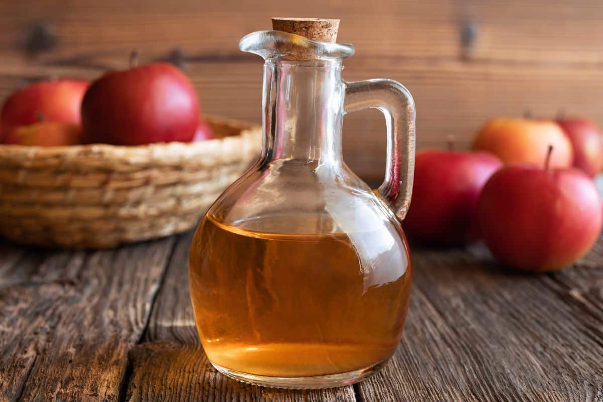 A jar of apple cider vinegar, a substitute for sherry, and apples on a wooden table.