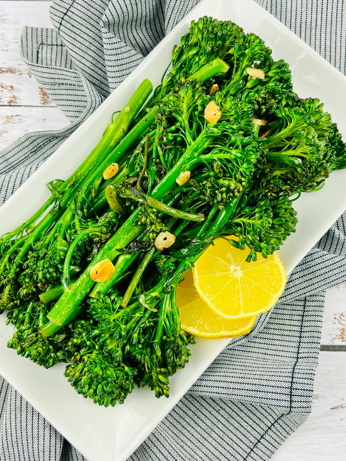 Overhead view of Tenderstem broccoli with garlic and lemon slices on a white serving platter.