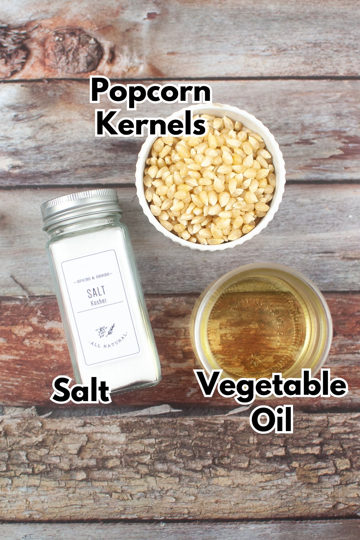 A bowl of popcorn kernels, vegetable oil and a jar of salt on a wooden surface.