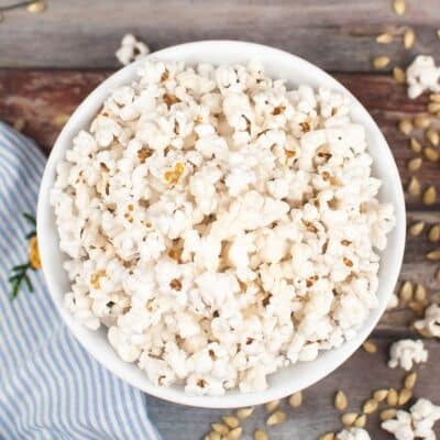 Bowl of freshly popped air fryer popcorn on a wooden surface with loose kernels scattered around.