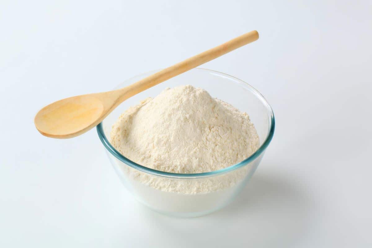 A wooden spoon resting on a glass bowl filled with all-purpose flour.