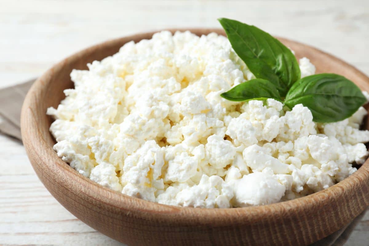 A bowl of fresh cottage cheese, a replacement for ricotta cheese, garnished with basil leaves.