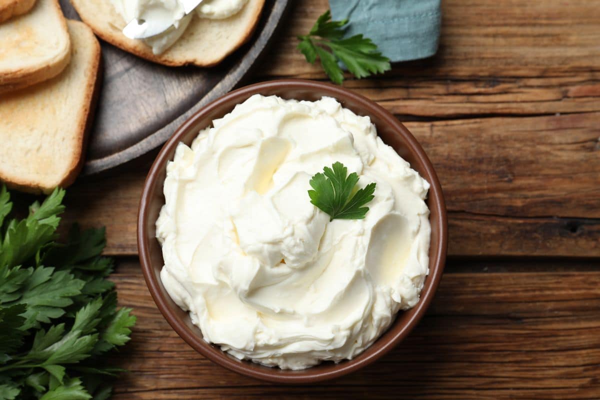 A bowl of cream cheese, a replacement for ricotta cheese, garnished with parsley on a wooden table.