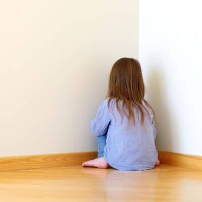 Child sitting on the floor facing a wall in the time out corner of a room.