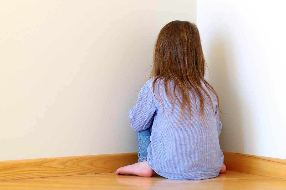A child sitting on the floor facing a wall in the time-out corner.