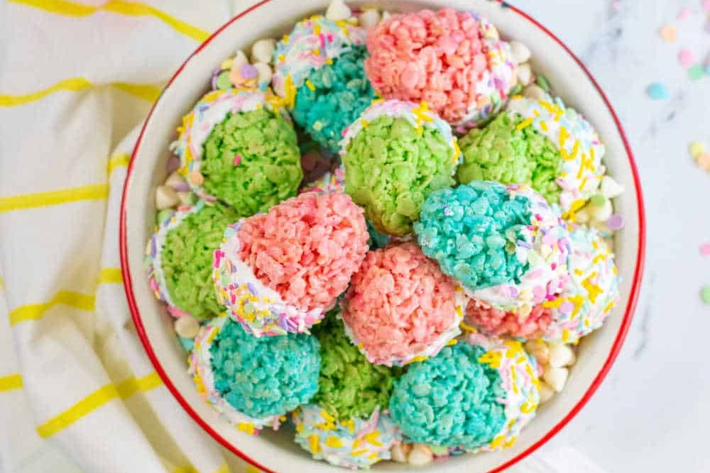A bowl of colorful rice cereal treats on a table with confetti.