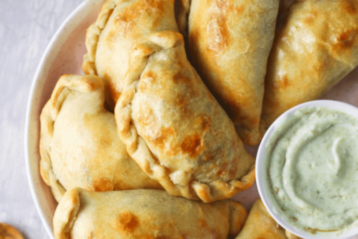 Golden-brown baked empanadas served with a side of green dipping sauce.