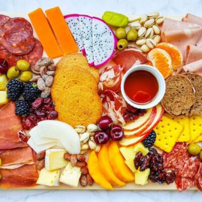 A charcuterie board with assorted meats, cheeses, fruits, nuts, crackers, and a small bowl of honey on a marble surface.
