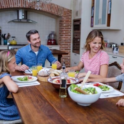 A family of four sits around a wooden table enjoying a meal together in a cozy kitchen setting.