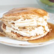 A stack of pancakes with whipped cream layers and syrup on a white plate.