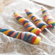Four colorful twisted lollipops on sticks rest on a sheet of crinkled wax paper.