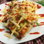 A serving of casserole topped with shredded cheese, chopped chives, and drizzled with red sauce on a white plate.