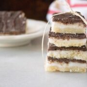 A stack of layered dessert bars with chocolate and cream filling tied with a string, with another bar on a plate in the background.