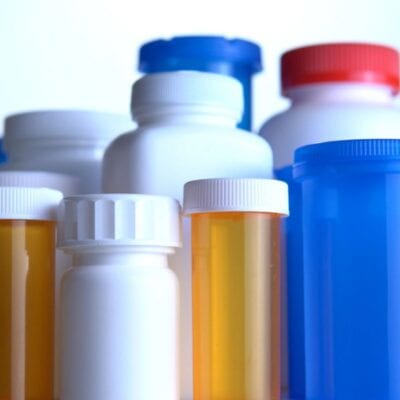 A collection of assorted prescription pill bottles and containers with white, orange, and blue colors, shown against a plain background.