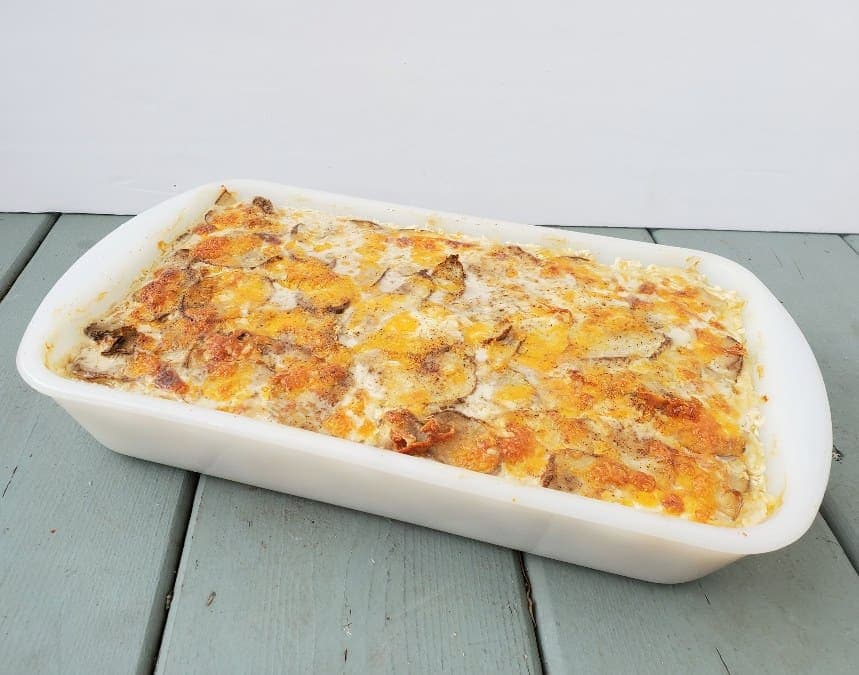 Scalloped potatoes topped with cheese in a white baking dish on a wooden table.