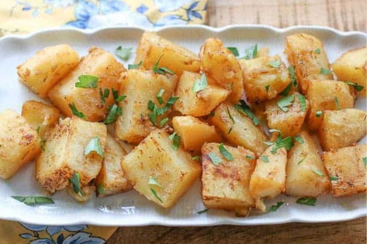Greek lemon potatoes on a white serving tray next to a yellow and blue cloth on a wood table.