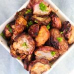 A bowl of roasted radishes garnished with chopped parsley, served in a white square dish on a light background.