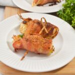 Three bacon-wrapped cabbage rolls secured with toothpicks are served on a white plate, garnished with herbs.