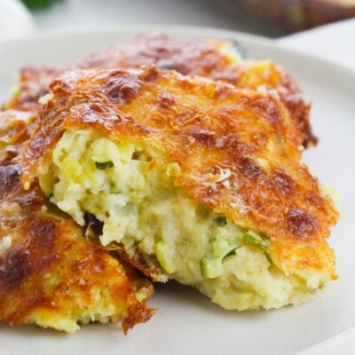 Close-up of two pieces of baked casserole with a golden-brown, cheesy crust and a creamy interior containing visible bits of zucchini.