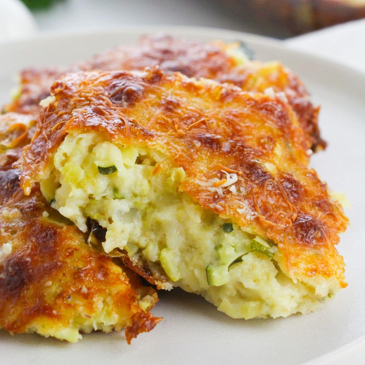 Close-up of two pieces of baked casserole with a golden-brown, cheesy crust and a creamy interior containing visible bits of zucchini.