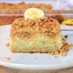 A slice of crumb-topped banana coffee cake on a white plate, garnished with a banana slice.