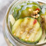 Close-up view of sliced pickles with mustard seeds and spices in a glass jar.