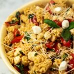 A bowl of pasta salad with cherry tomatoes, mozzarella balls, fresh basil, and grated parmesan cheese.